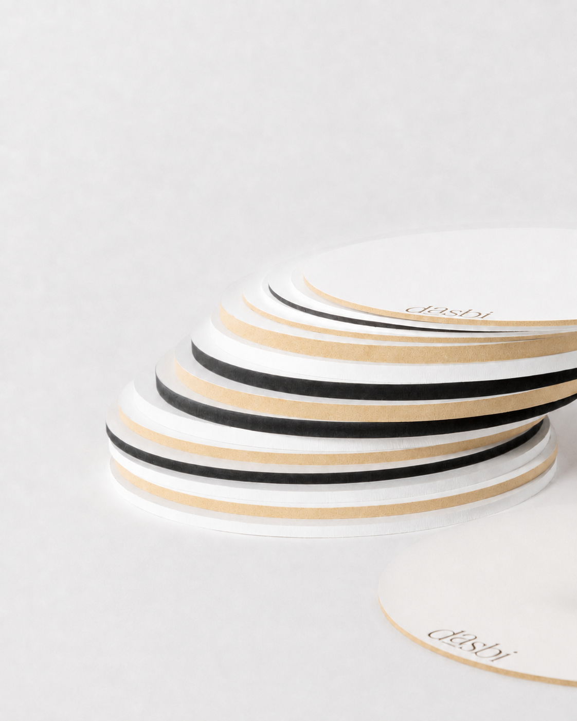 A stack of round white paper coasters with alternating black and beige stripes, photographed on a clean white background. The word 'dushi' is printed in a thin black script on the top surface of the coasters.