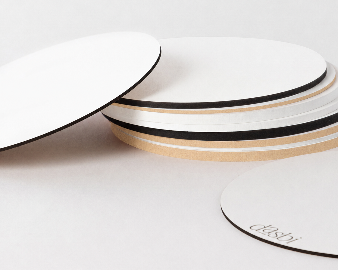 A stack of minimalist round coasters with a white top surface, black side edge, and natural wood base, photographed on a clean white background.