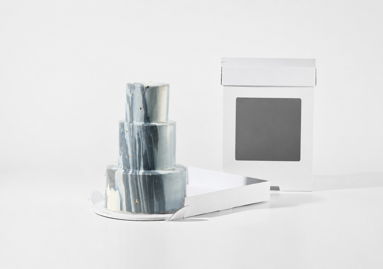 A three-tiered cake with a metallic silver and gray marbled pattern, displayed next to its white cardboard packaging box on a seamless white background.
