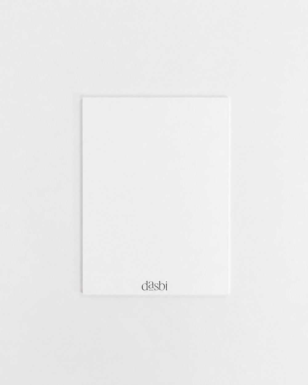 A minimalist white rectangular card or notebook cover with the brand name 'dasbi' printed in a small black serif font at the bottom, centered on a light gray background.