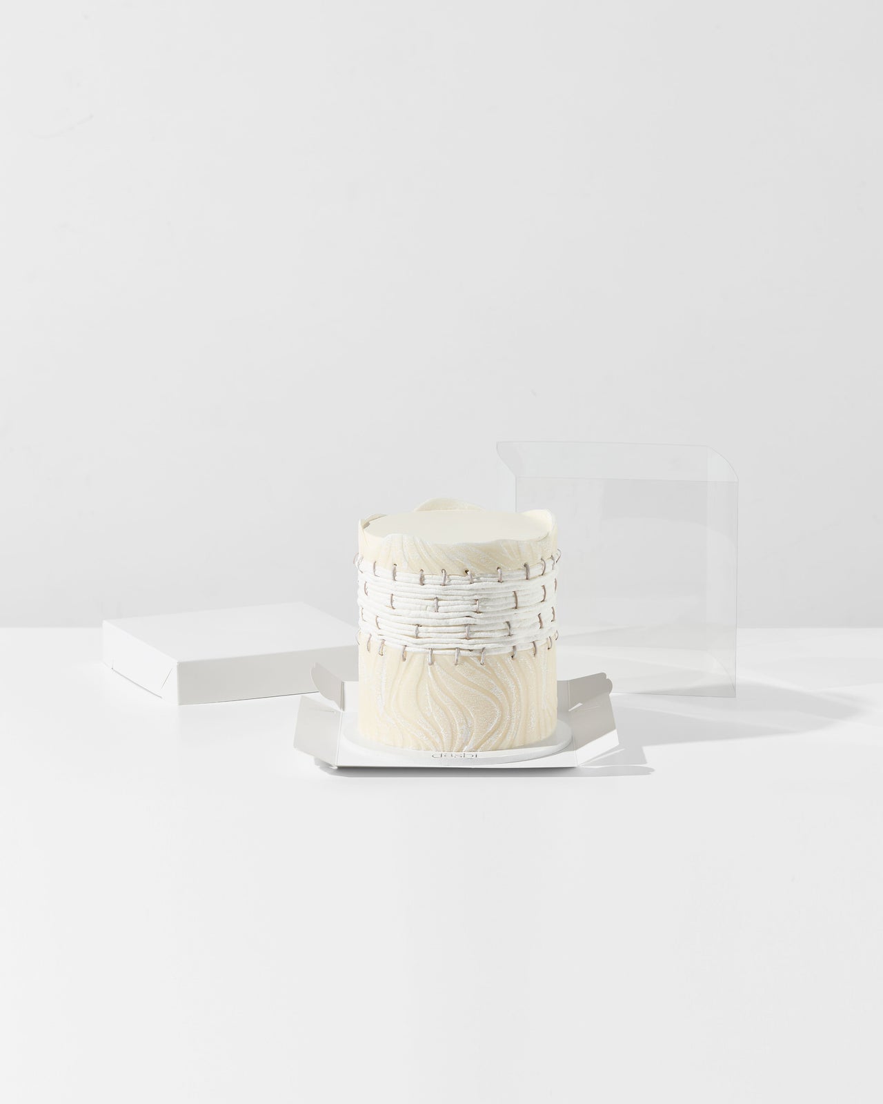 Small white cake with decorative elements on a white plate against a white background