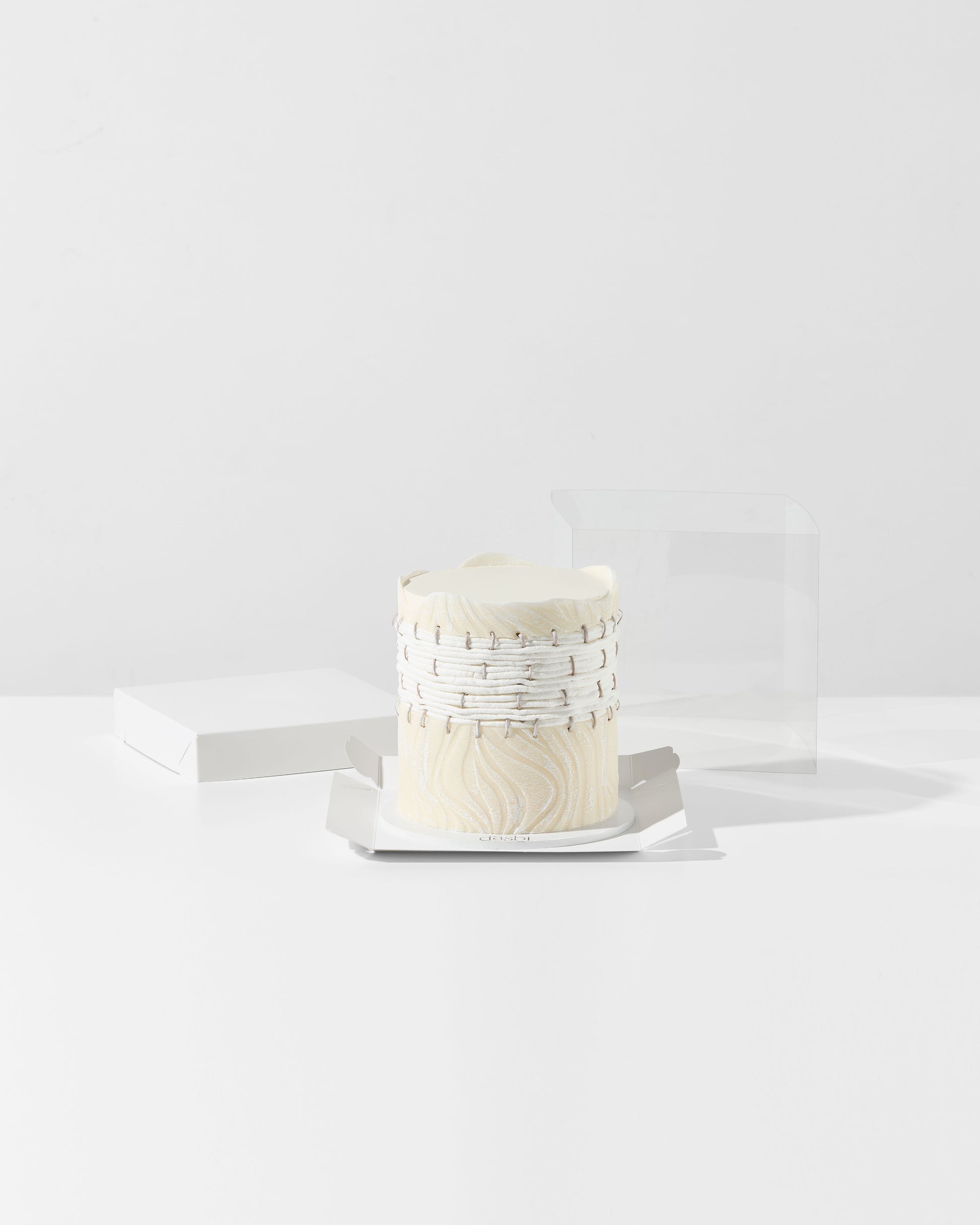 Small white cake with decorative elements on a white plate against a white background